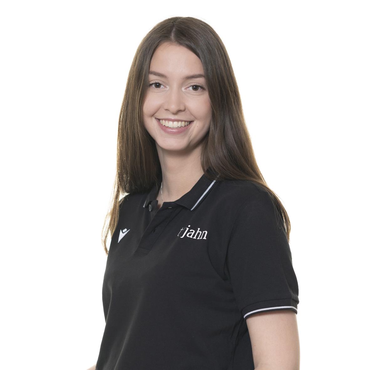 Portr&auml;t einer l&auml;chelnden Frau mit langen, braunen Haaren in einem schwarzen Poloshirt vor wei&szlig;em Hintergrund.