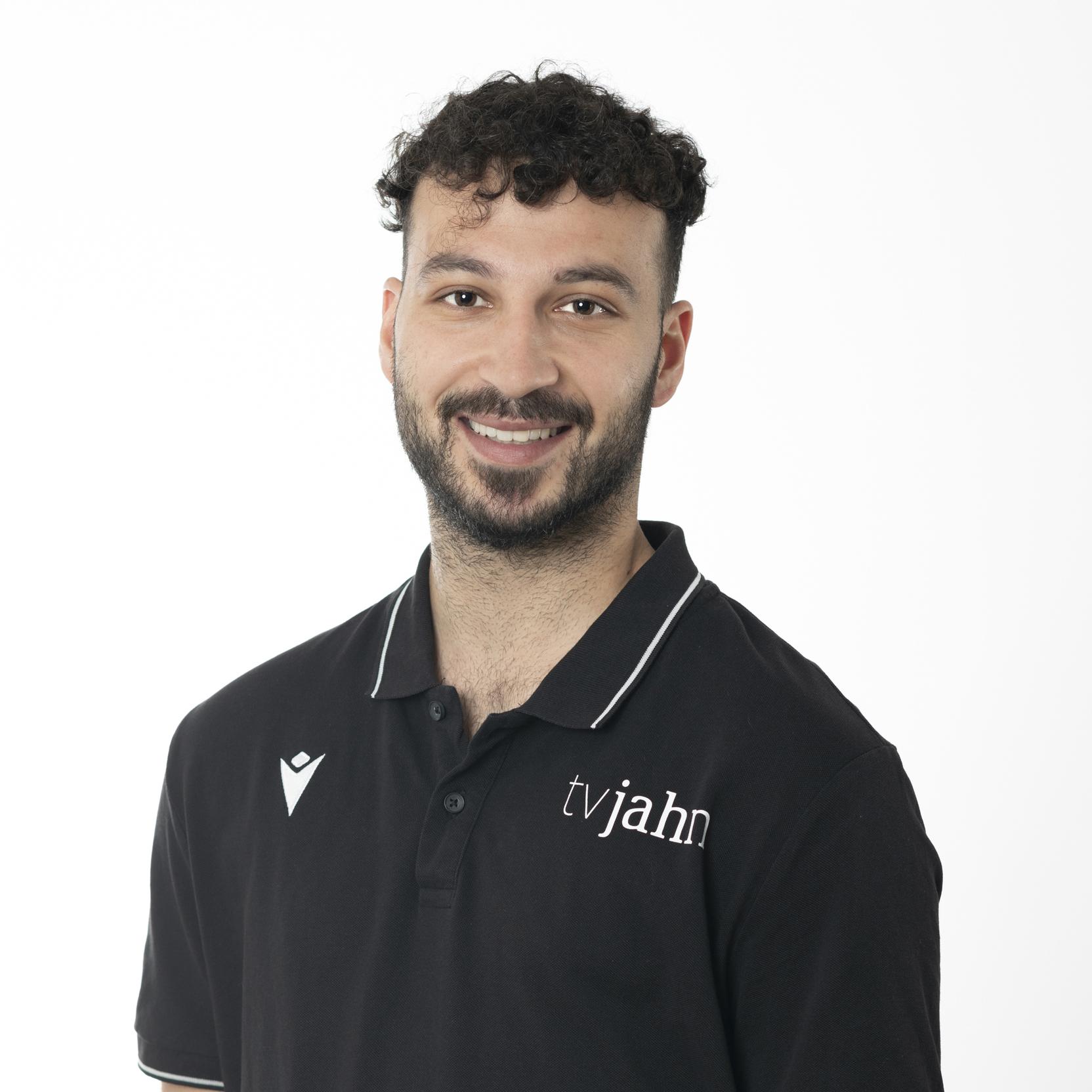 Portrait eines l&auml;chelnden Mannes mit kurzen dunklen Haaren, in einem schwarzen Poloshirt mit logo. Wei&szlig;er Hintergrund.