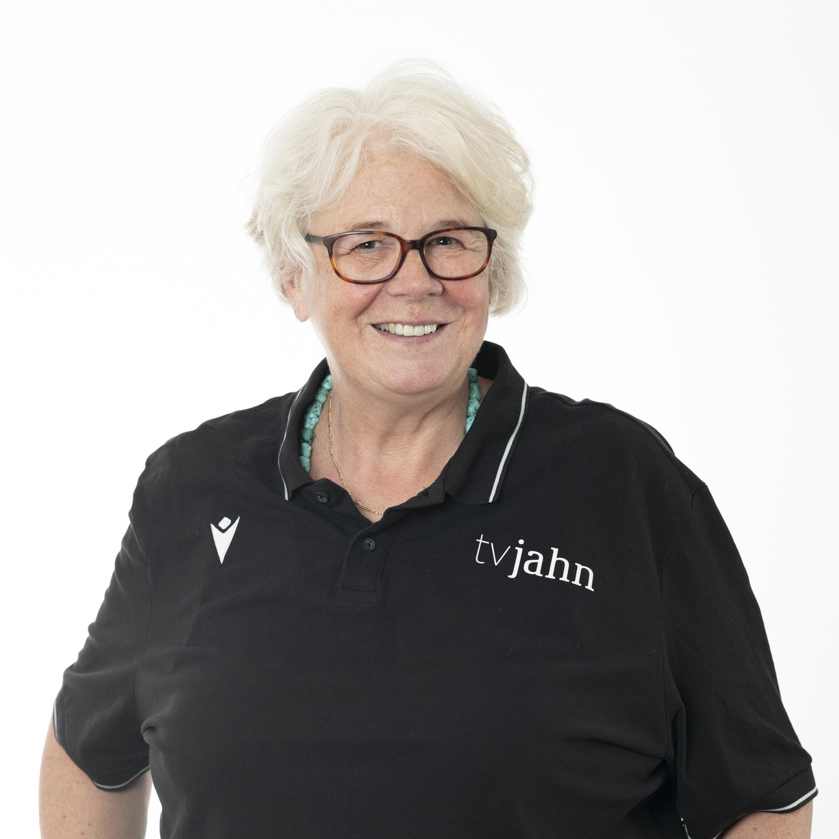 Porträt einer lächelnden Frau mit Brille, die ein schwarzes Polo-Shirt mit dem Logo „tvjahn“ trägt.