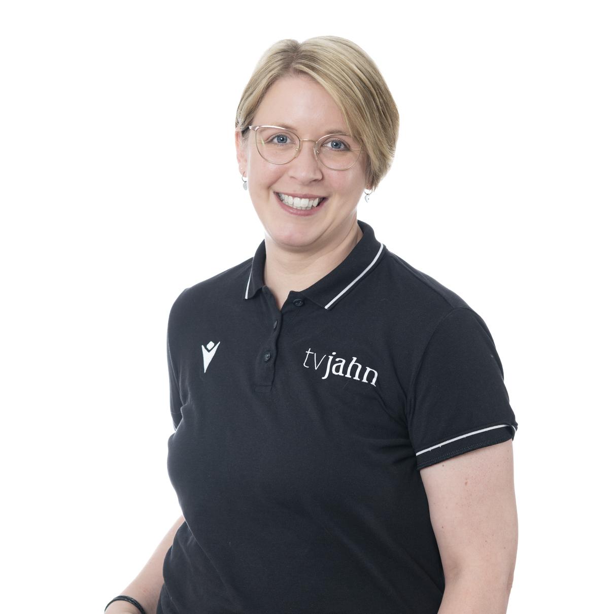 L&auml;chelnde Frau mit kurzen blonden Haaren, tr&auml;gt ein schwarzes Poloshirt mit dem Schriftzug "tv jahn".