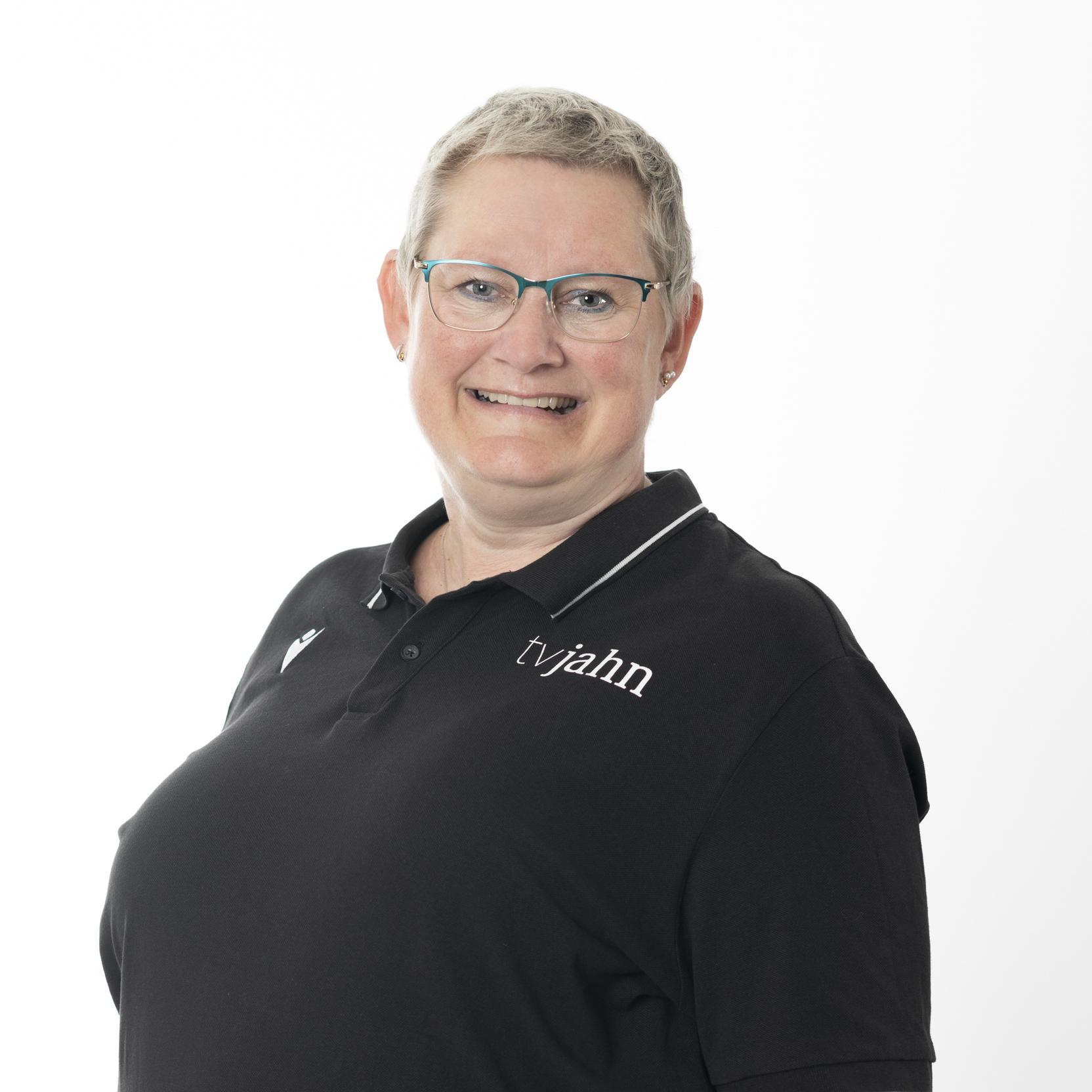 Portr&auml;t einer l&auml;chelnden Frau mit Kurzhaarschnitt, Brille und schwarzem Poloshirt mit Logo auf wei&szlig;em Hintergrund.