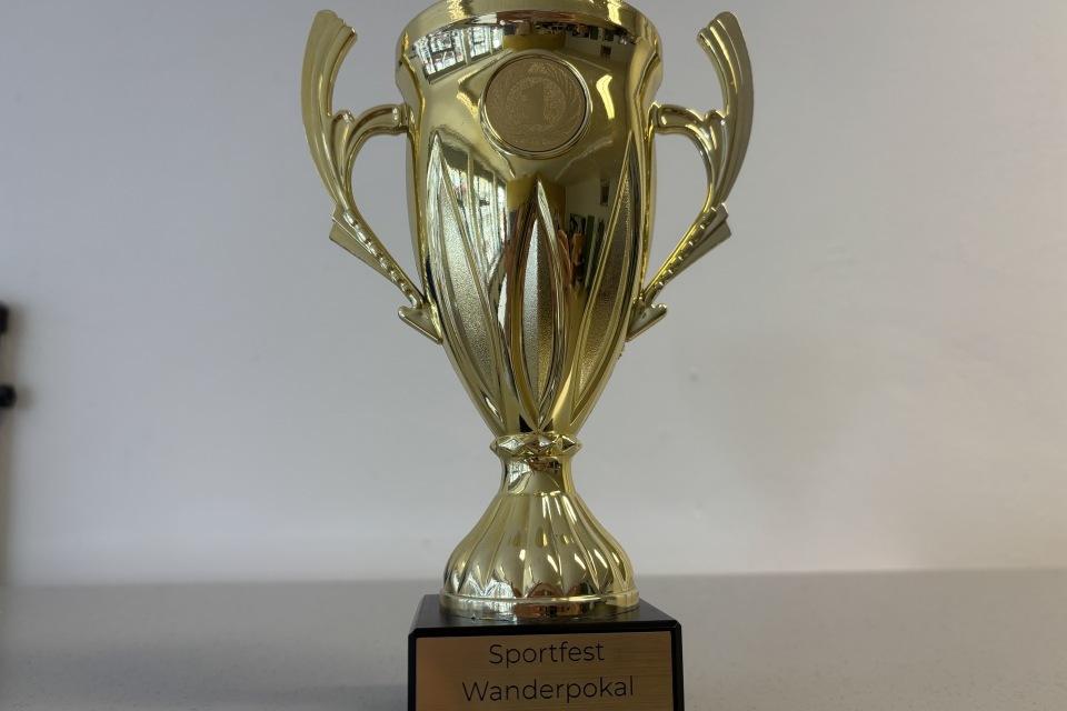 Goldener Wanderpokal mit der Inschrift "Sportfest Wanderpokal TV Jahn Rheine" auf einem schwarzen Sockel.