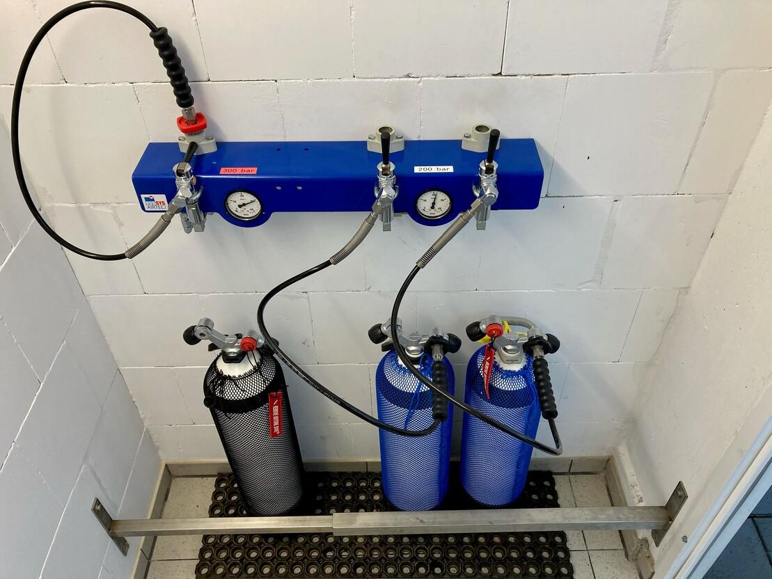 Ausr&uuml;stung zur Atemluftversorgung mit Druckanzeigen und zwei Flaschen an einer Wandhalterung in einem Raum.