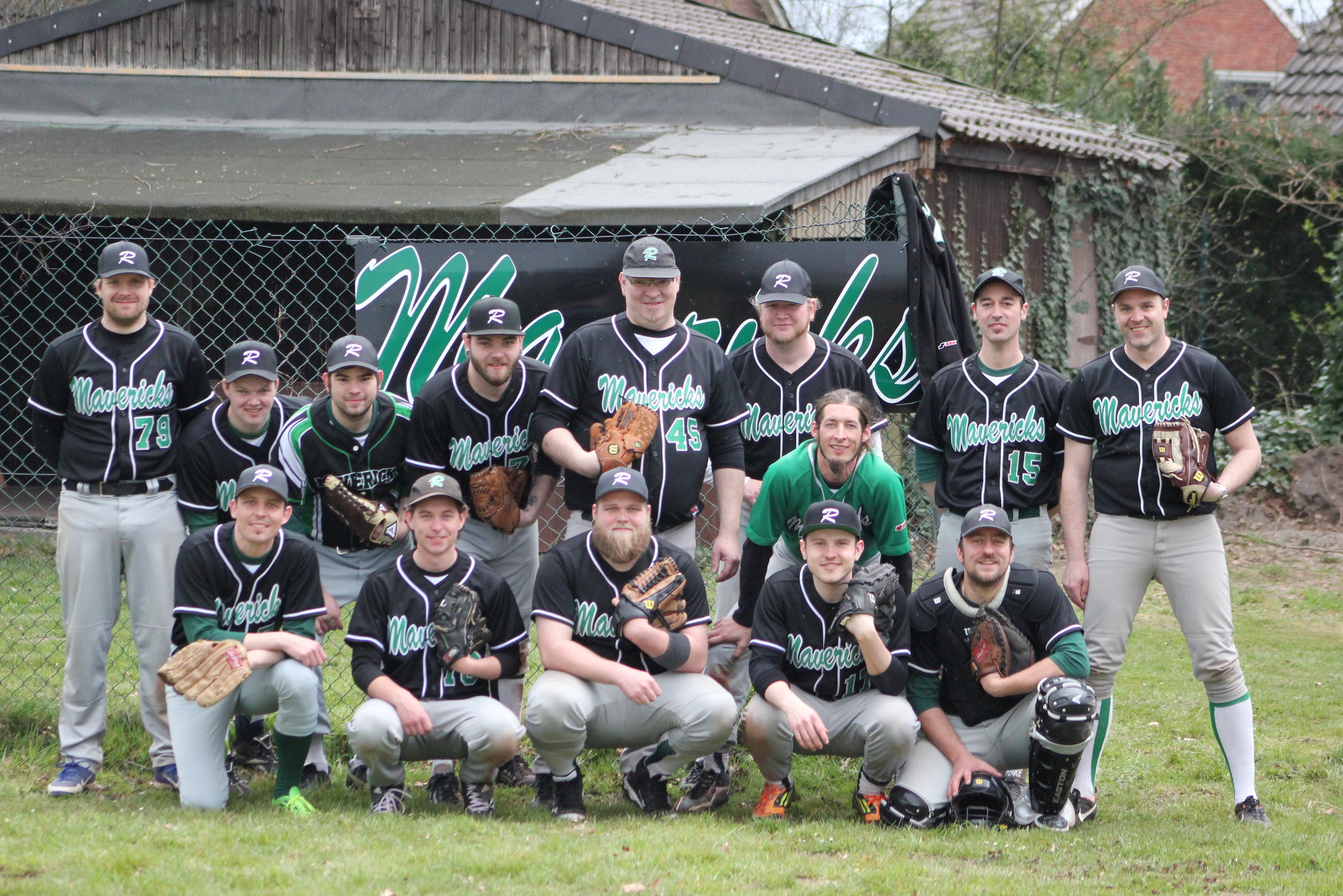 Gruppensportrait von 14 Baseballspielern in schwarzen Trikots mit wei&szlig;en und gr&uuml;nen Details auf einem Sportplatz.