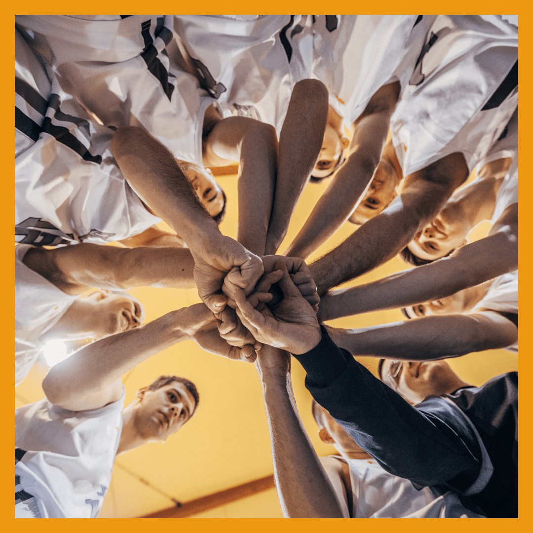 Zehn Hände in einem Huddle, die sich in der Mitte treffen, um den Teamgeist im Basketball zu symbolisieren.