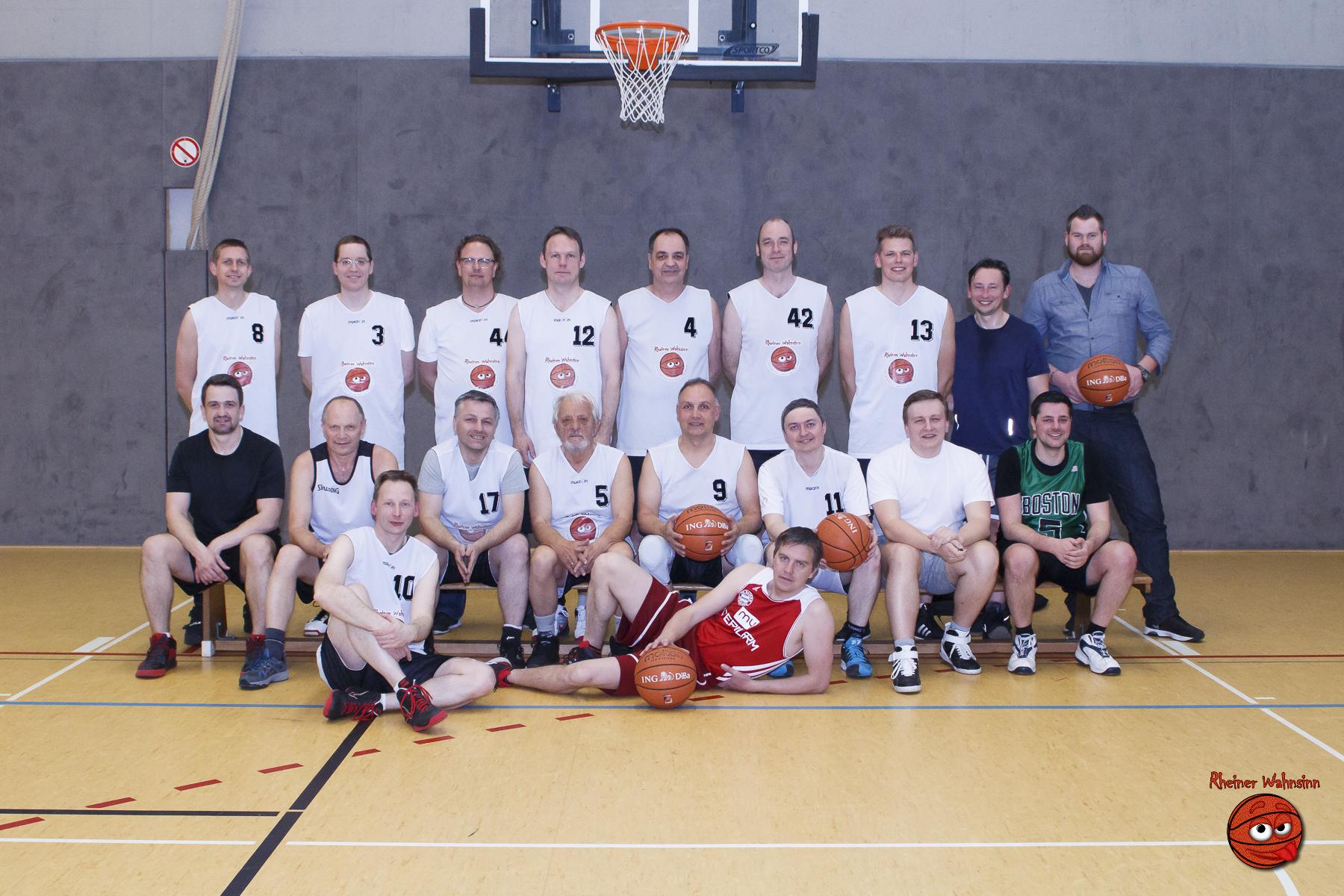 Gruppenfoto von 17 Basketballspielern in Trikots mit Nummern, posed auf einem Basketballplatz mit Bällen.