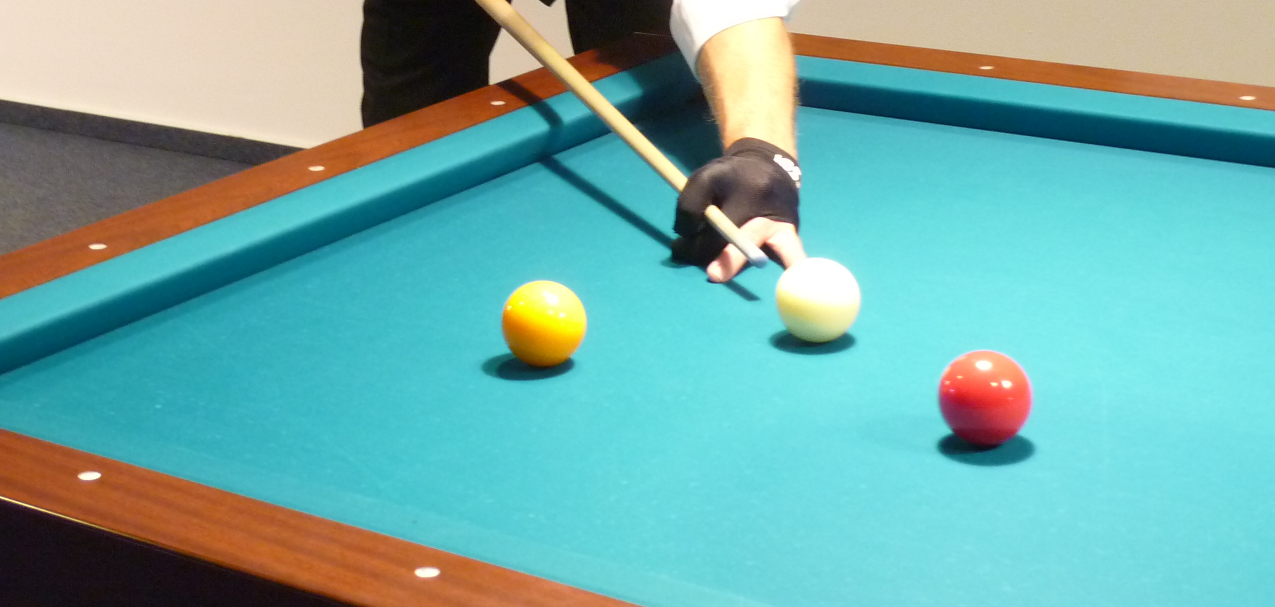 Mann mit Brille und Weste spielt Billard und zielt mit einem Queue auf die Kugeln auf einem gr&uuml;nen Tisch.