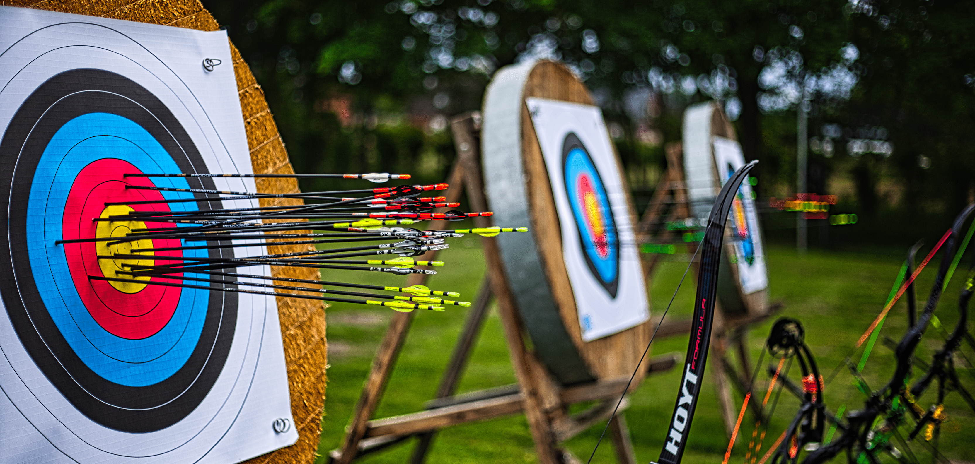 Nahaufnahme von drei Zielscheiben mit zahlreichen Pfeilen auf einem Sportplatz für Bogenschießen.