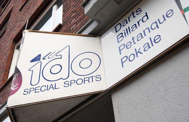Schild mit der Aufschrift &bdquo;1do Special Sports&ldquo; und Sportarten wie Darts, Billard, Petanque und Pokale.