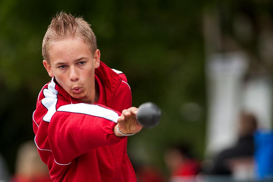 Junge im roten Sportanzug voll konzentriert beim Werfen eines Balls in einem Wettkampf.