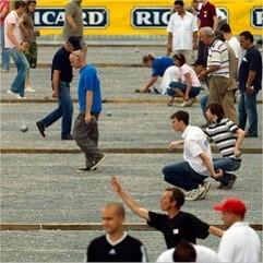 Menschen spielen Boule auf einem Platz, w&auml;hrend Zuschauer das Geschehen aufmerksam verfolgen.