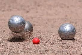 Drei silberne Boulekugeln und eine rote Zielkugel liegen im Sand auf einem Bouleplatz.