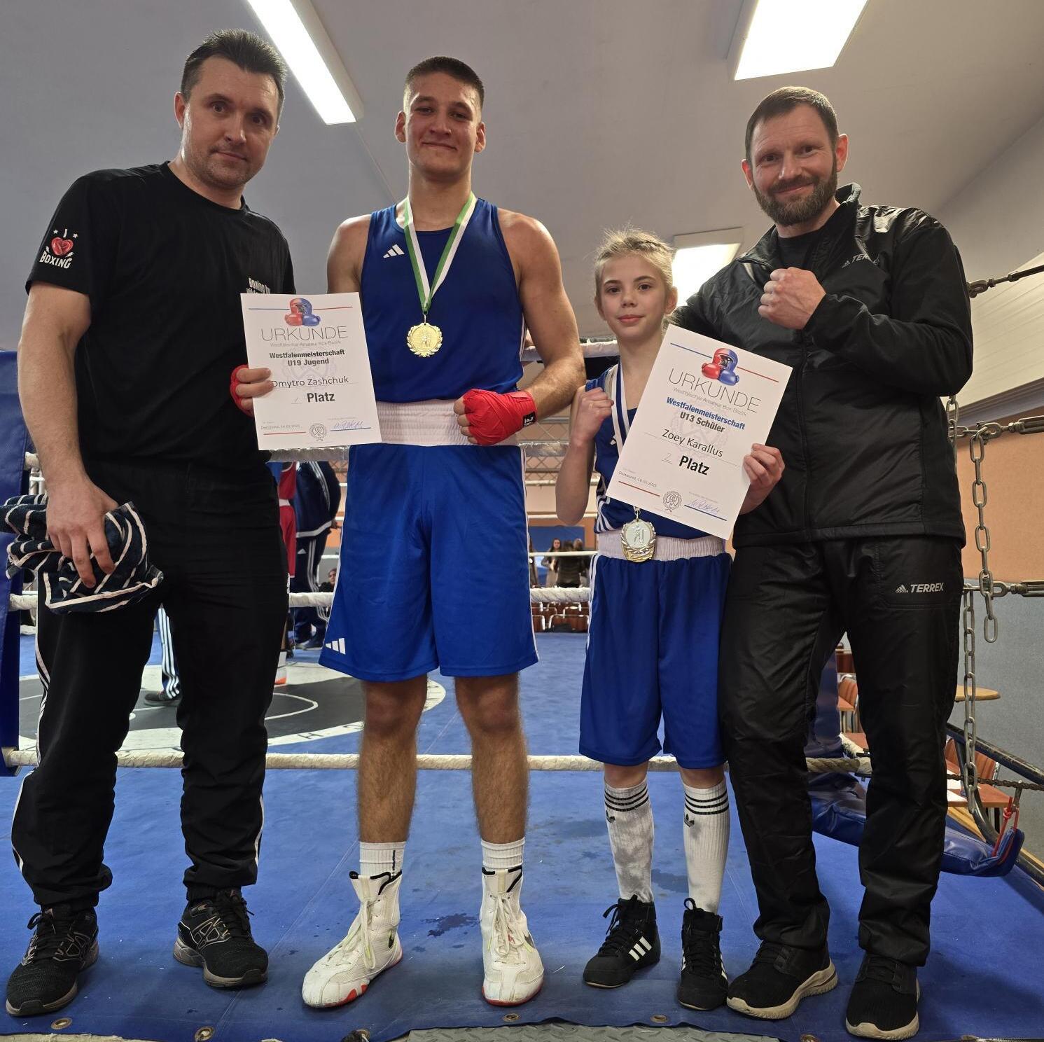 Vier Personen in Trainingskleidung stehen in einem Boxring, halten Urkunden für ihre Platzierungen in den Händen.