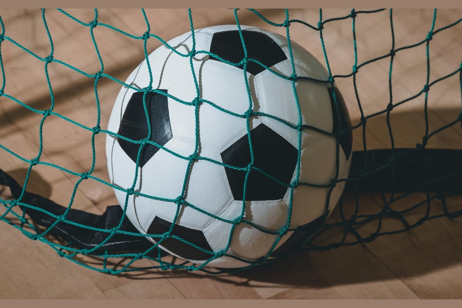 Nahaufnahme eines Fußballs, der im Netz eines Fußballtores liegt.