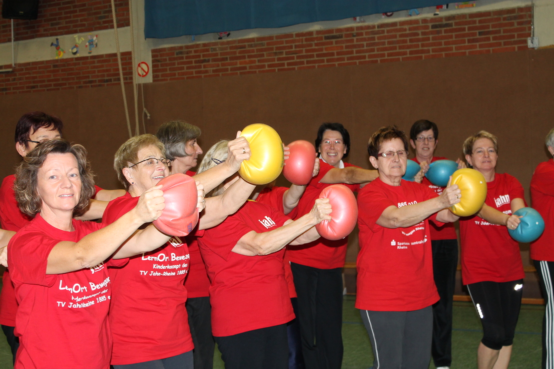 Gruppe von Frauen in roten T-Shirts, die mit Hanteln in verschiedenen Farben trainieren.