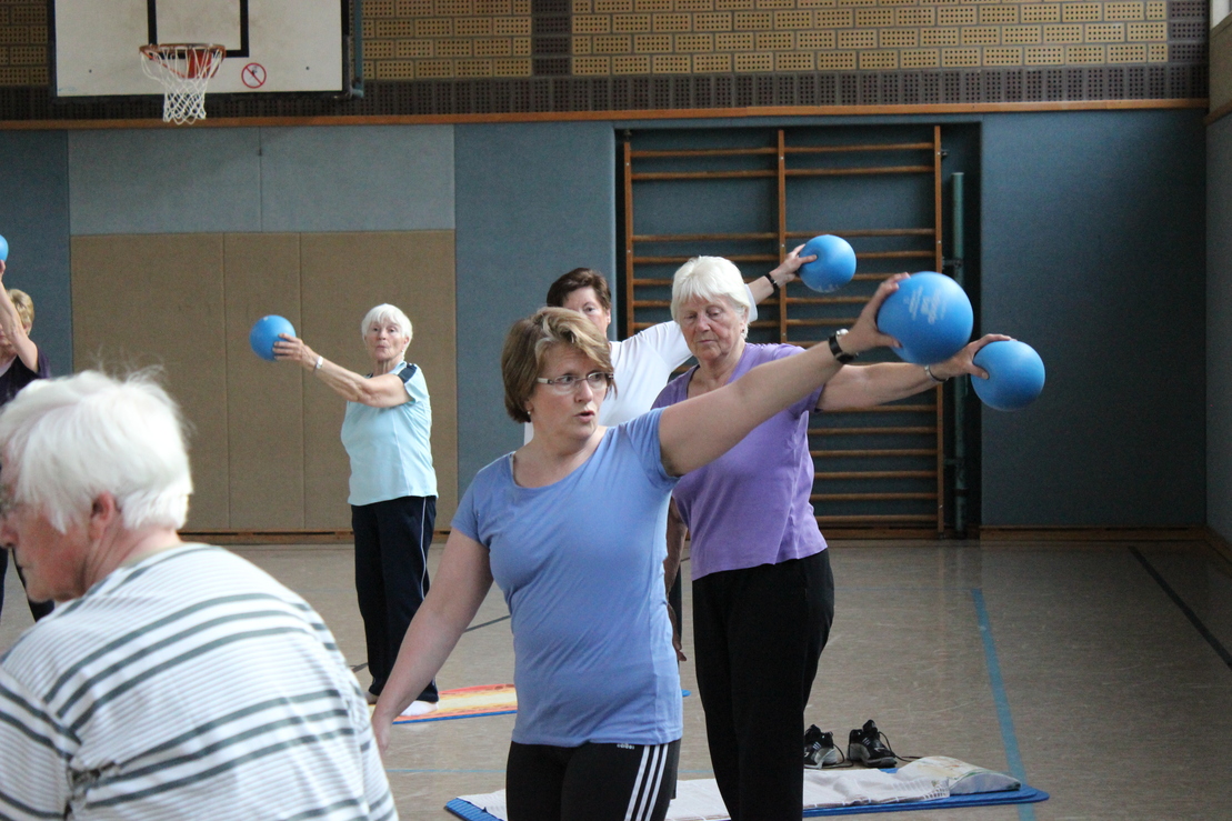 Gruppe &auml;lterer Frauen und M&auml;nner beim Fitness mit kleinen blauen B&auml;llen in einer Sporthalle.