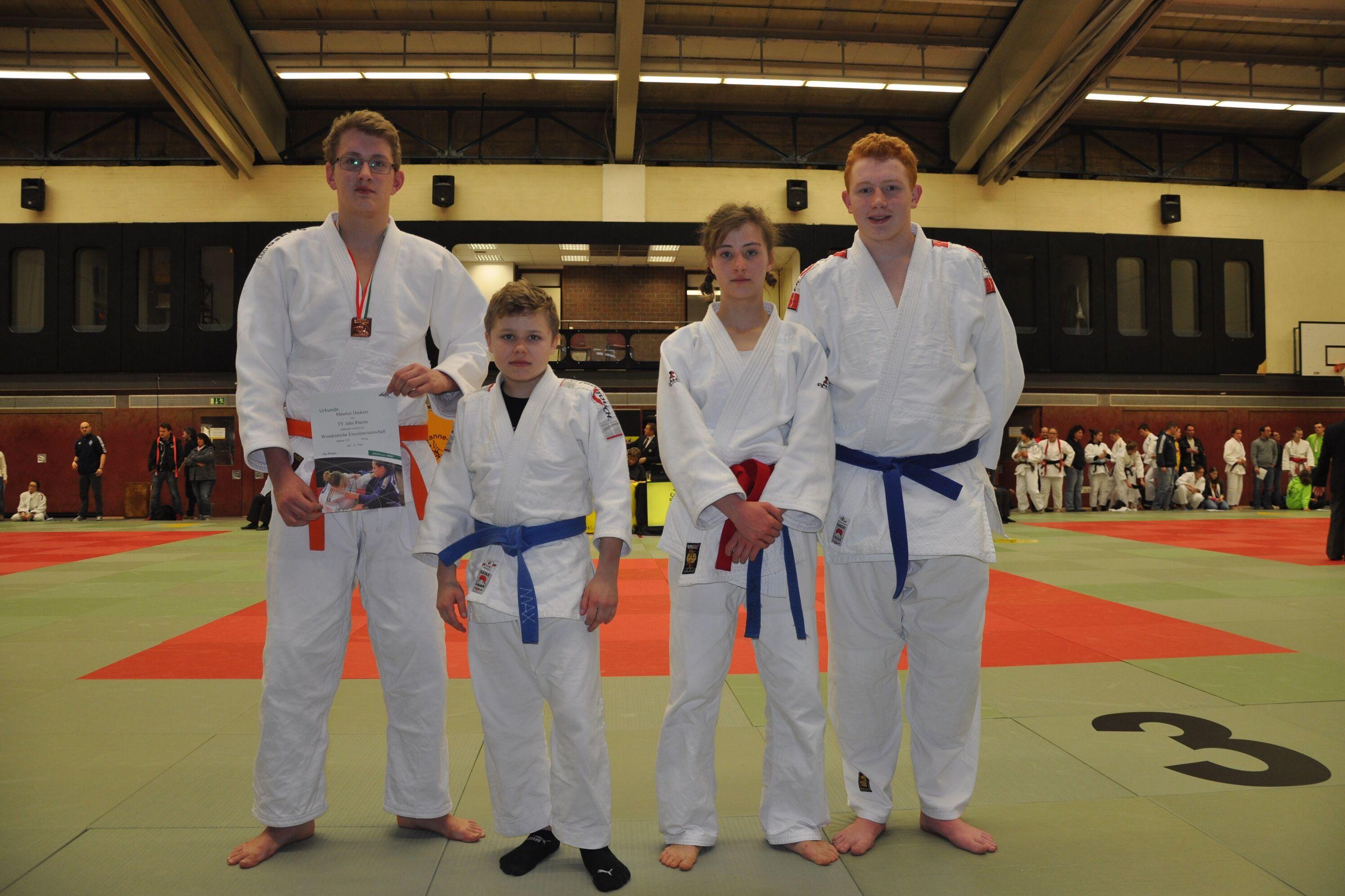 Vier Judoka in wei&szlig;en und blauen Judogis stehen auf einer Tatami, l&auml;chelnd nach einem Wettkampf.