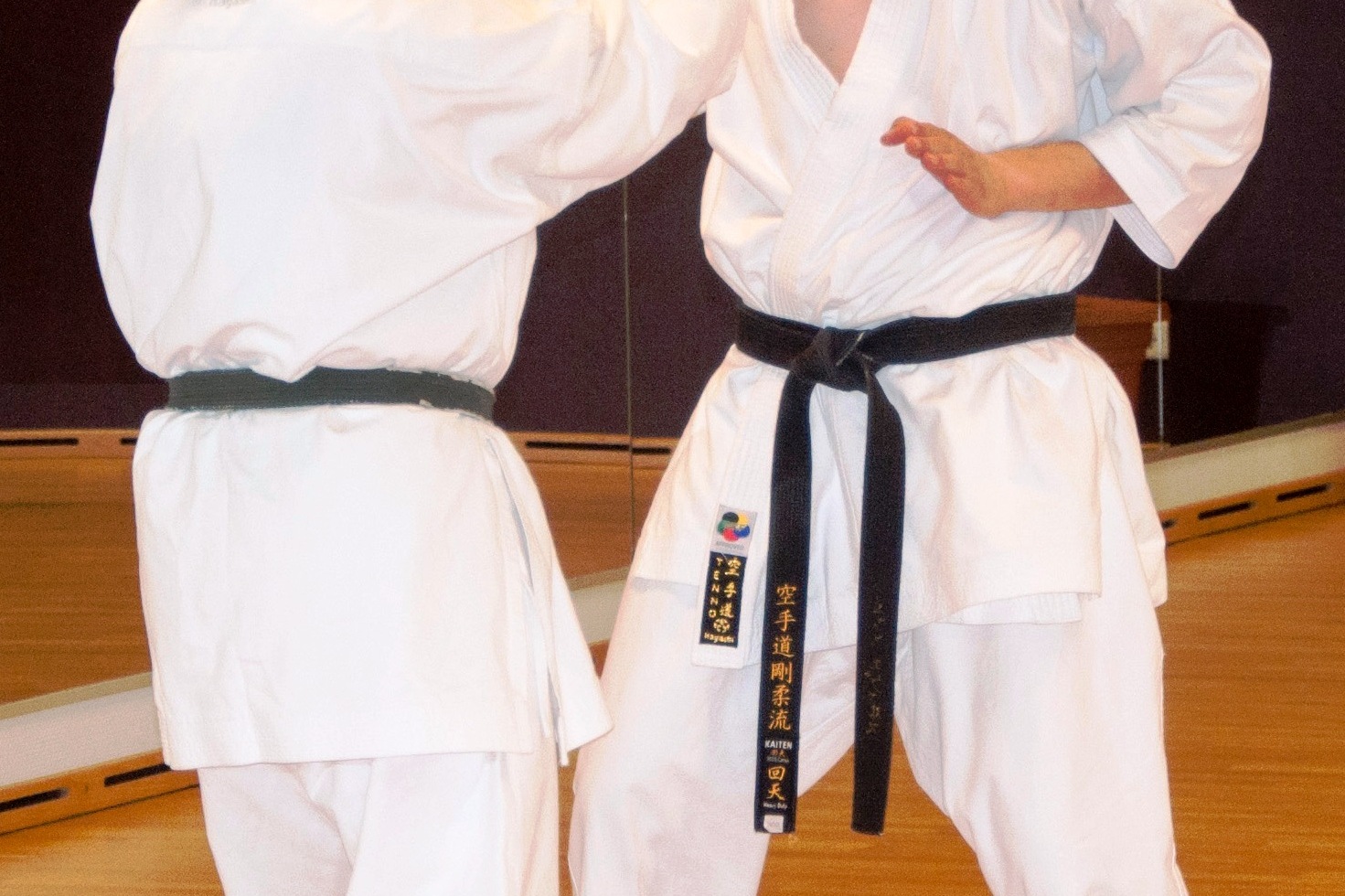 Zwei Karateka in Wei&szlig; und Schwarz &uuml;ben Techniken in einem Trainingsraum mit Spiegelw&auml;nden.