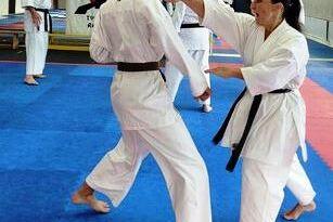 Zwei Karateka in wei&szlig;en Anz&uuml;gen &uuml;ben Techniken auf einer blauen und roten Mattenfl&auml;che in einem Dojo.