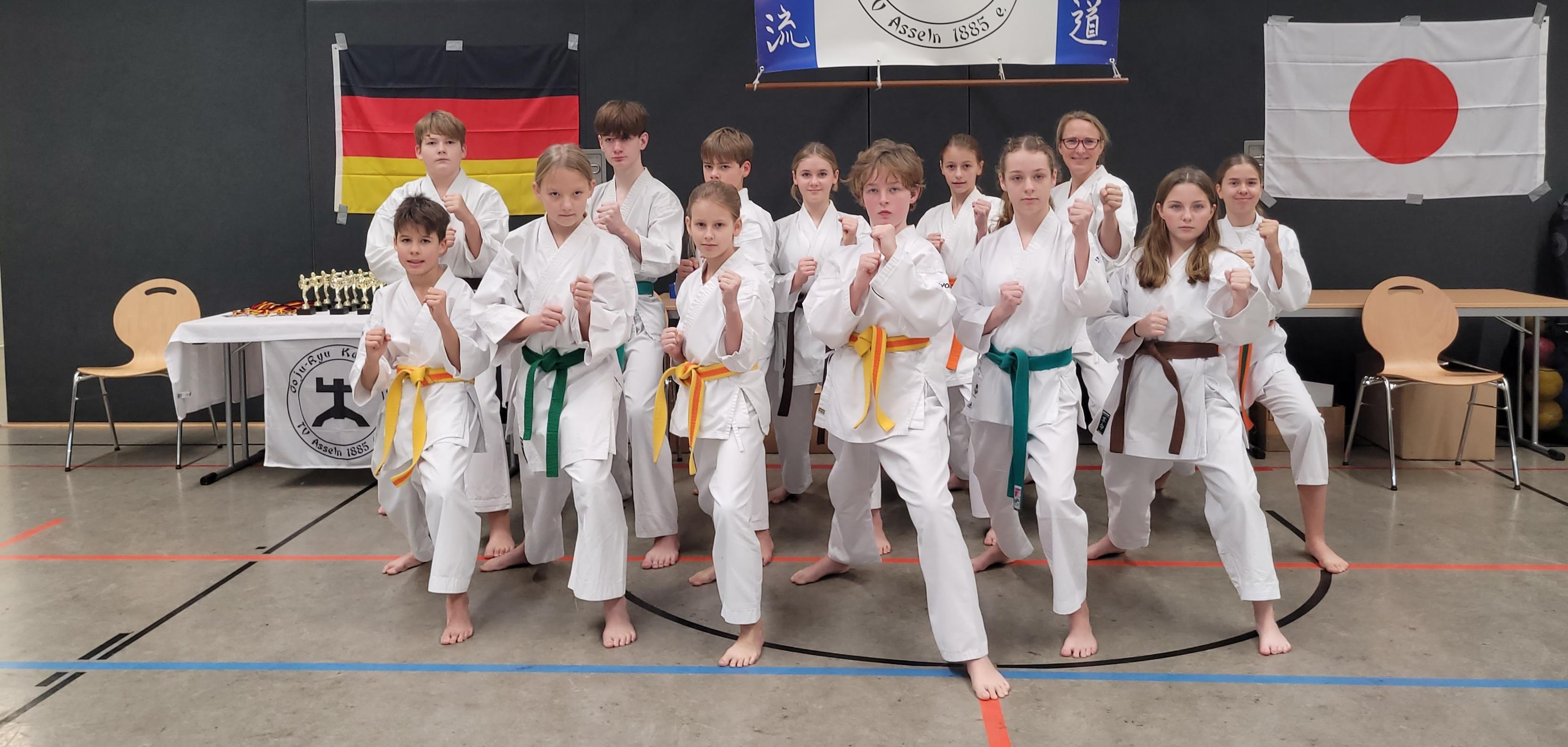 Gruppe junger Karateka in wei&szlig;en Anz&uuml;gen zeigt Kampfstellung vor Flaggen von Deutschland und Japan.