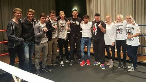 Gruppe von zehn Personen im Boxring, l&auml;chelnd und posierend, in Sportkleidung und mit Boxhandschuhen.