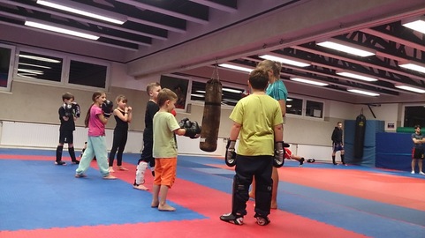 Gruppe von Kindern in Trainingskleidung im Kampfsportstudio mit einem Boxsack und Trainer.