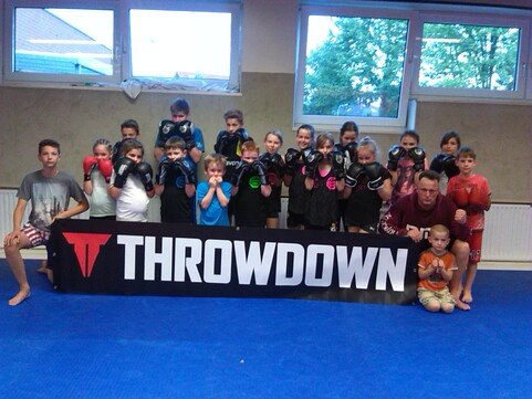 Gruppe von Kindern und Jugendlichen mit Boxhandschuhen, die vor einem THROWDOWN-Banner auf einer blauen Matte posiert.