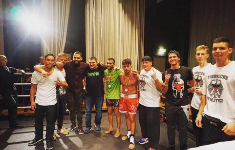 Gruppe von neun Personen in Sportkleidung, einige tragen Medaillen, nach einem Wettkampf in einer Halle.