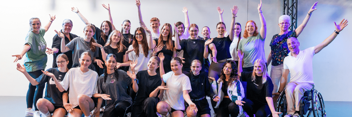Gruppenselfie von 20 Personen in sportlicher Kleidung, die fr&ouml;hlich mit erhobenen H&auml;nden posieren.