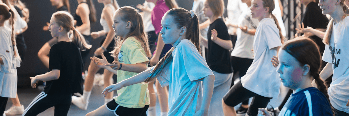 Gruppe von Kindern tanzt synchron in einem Raum mit buntem Licht, einige tragen Sportkleidung.