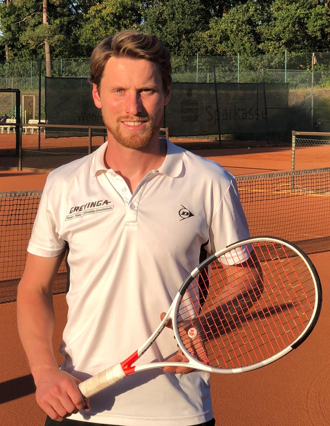 Junger Mann h&auml;lt einen Tennisschl&auml;ger in sportlicher Kleidung auf einem Tennisplatz mit Sandboden.