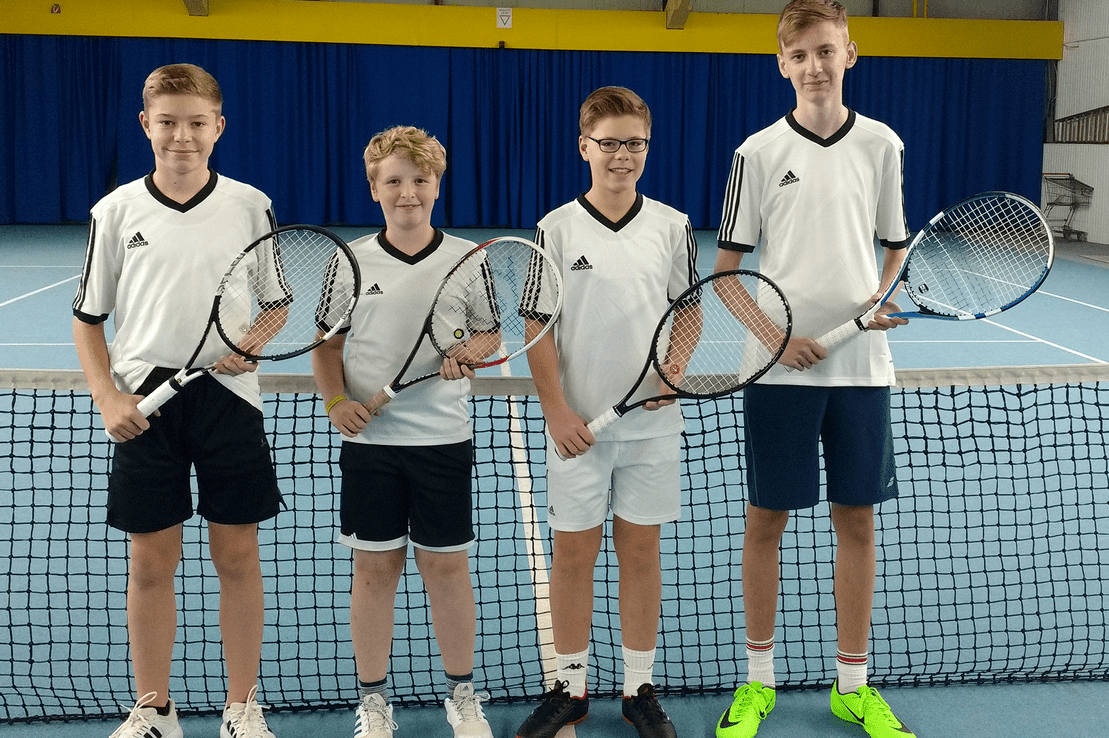 Vier Jugendliche in Sportkleidung stehen am Netz eines Tennisplatzes, jeder mit einem Tennisschl&auml;ger in der Hand.
