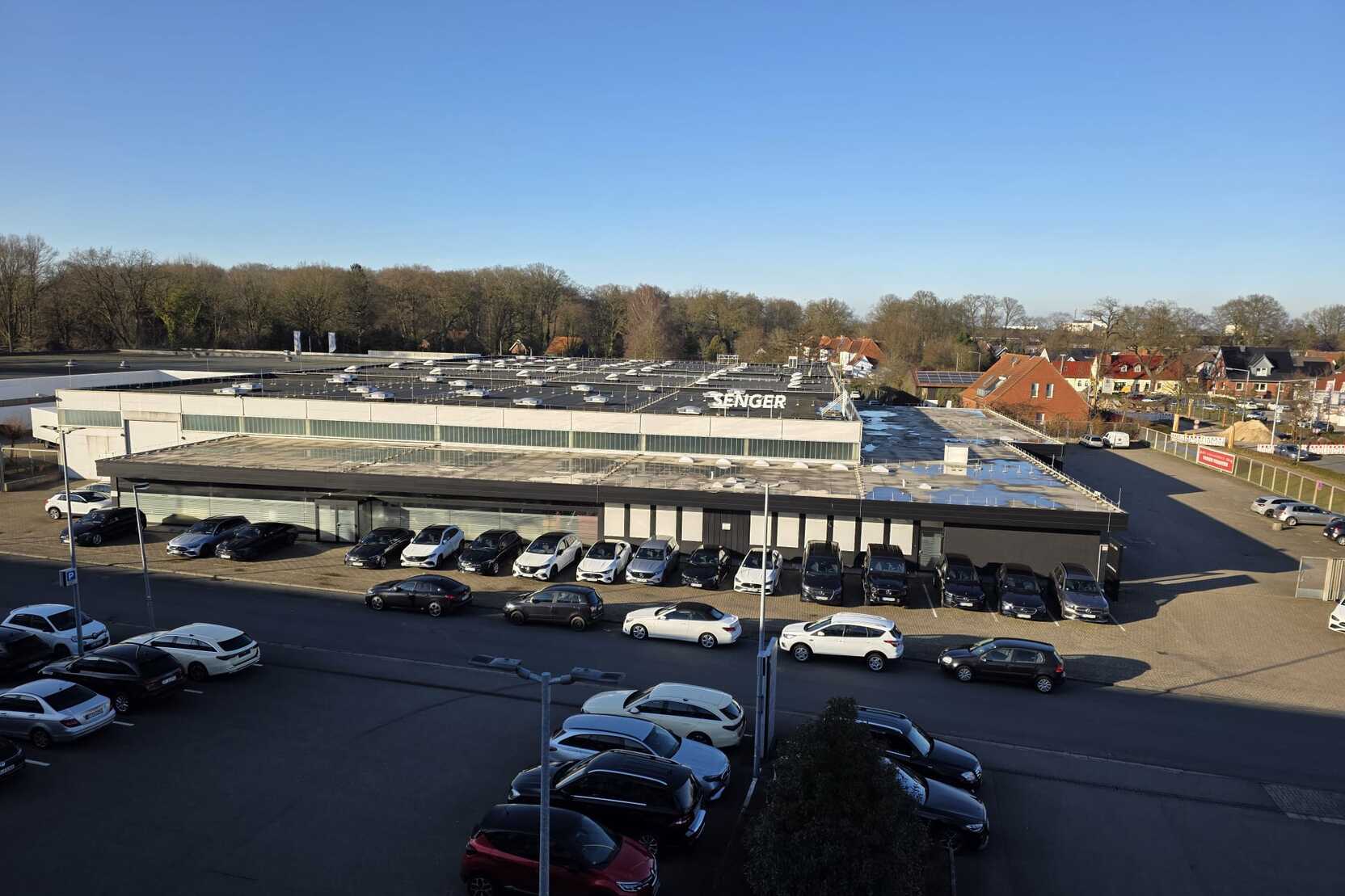 Blick auf ein gro&szlig;es Gesch&auml;ftsgeb&auml;ude mit vielen geparkten Autos und einem blauen Himmel im Hintergrund.