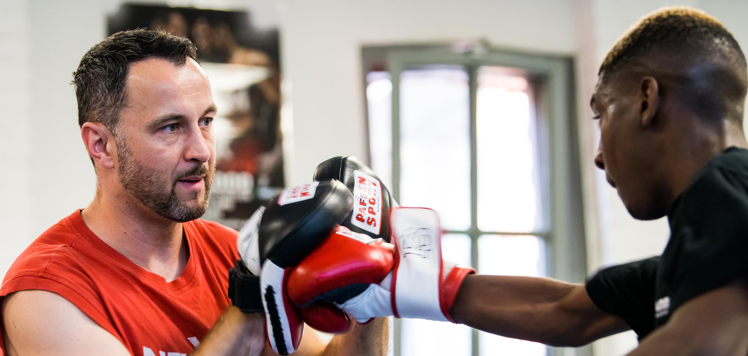 Trainer überwacht das Boxtraining eines Schülers, beide tragen Boxhandschuhe in einem Trainingsraum.