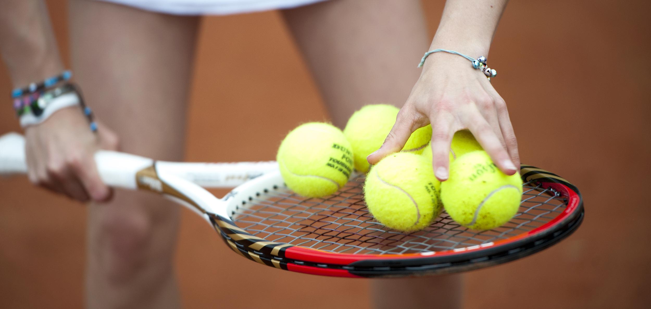 Hand greift mehrere gelbe Tennisbälle auf einem Tennisschläger, während die andere Hand die Schlägerhaltung stabilisiert.
